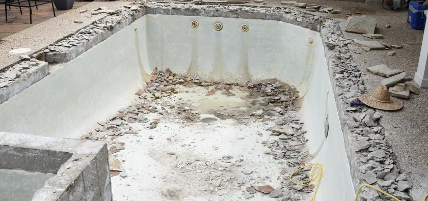 Pool demolition in Dallas TX with empty pool and debris removal process in progress