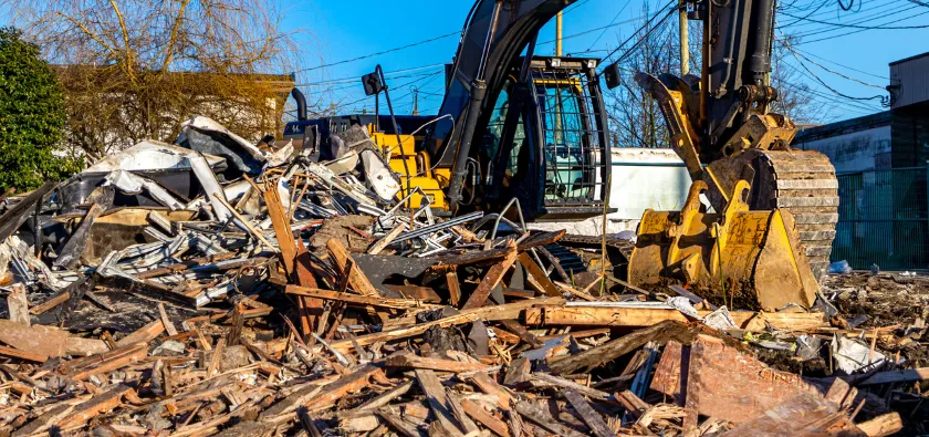 Residential demolition in Dallas TX with excavator clearing debris and wood materials after house teardown