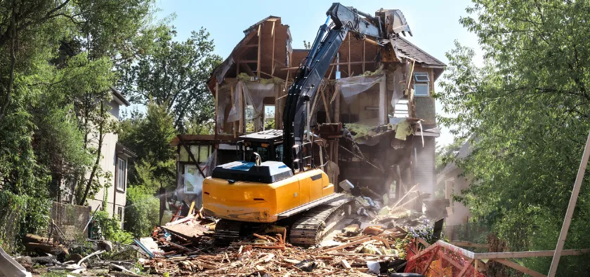 Residential demolition in Dallas TX showing excavator tearing down house structure during full demolition project
