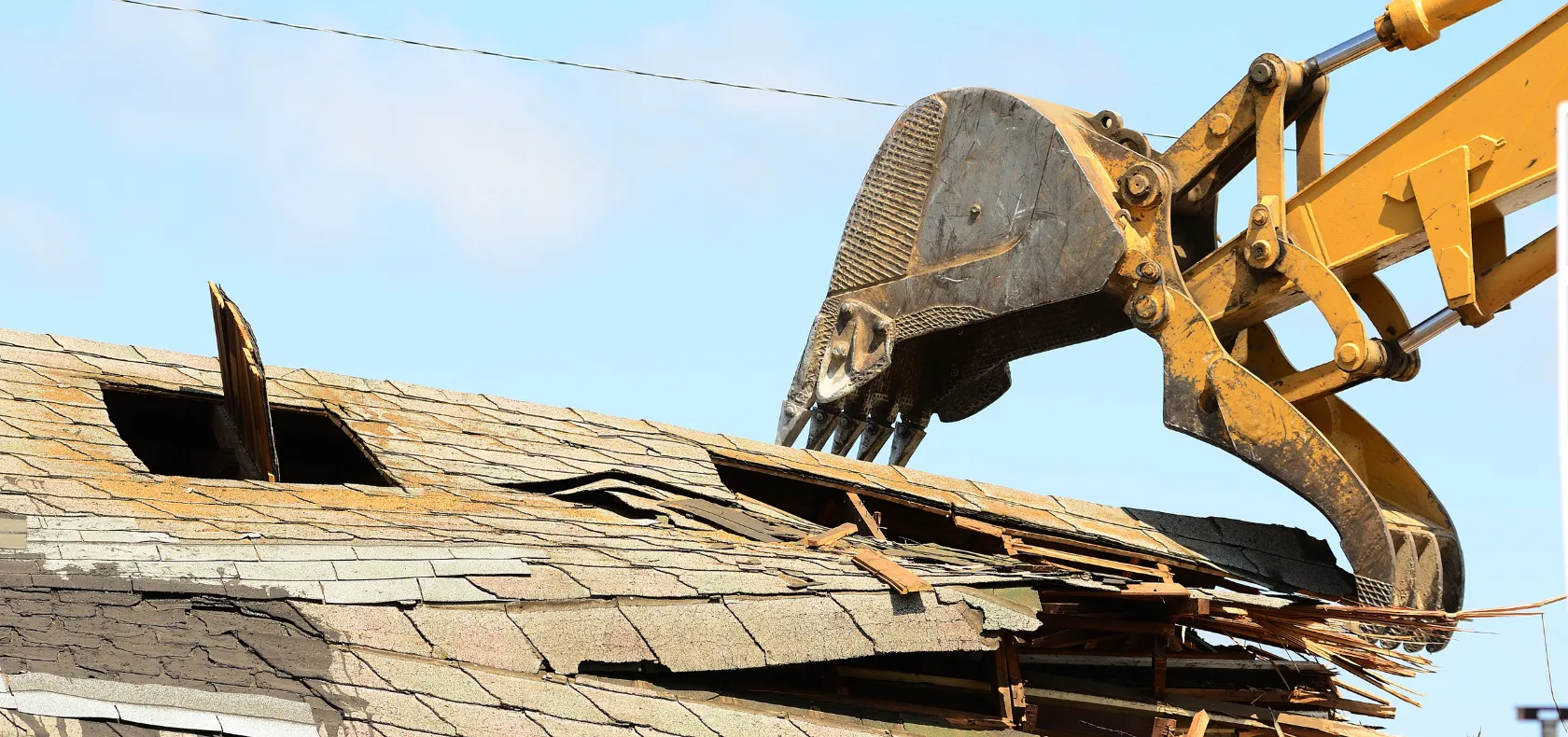 Residential demolition in Dallas TX with excavator removing roof structure during house teardown project